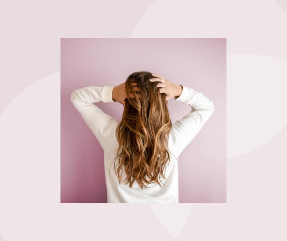 A young woman with her back to camera fluffs her long brown hair with her hands.