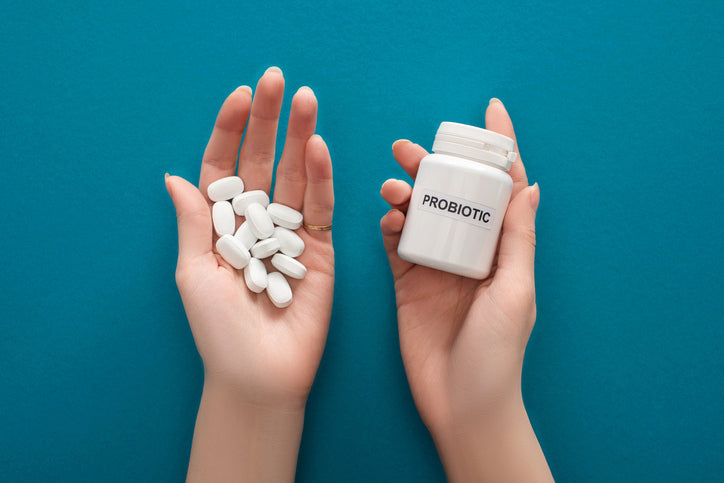 A cropped image of a woman holding a white probiotic container and pills in hands on blue background.