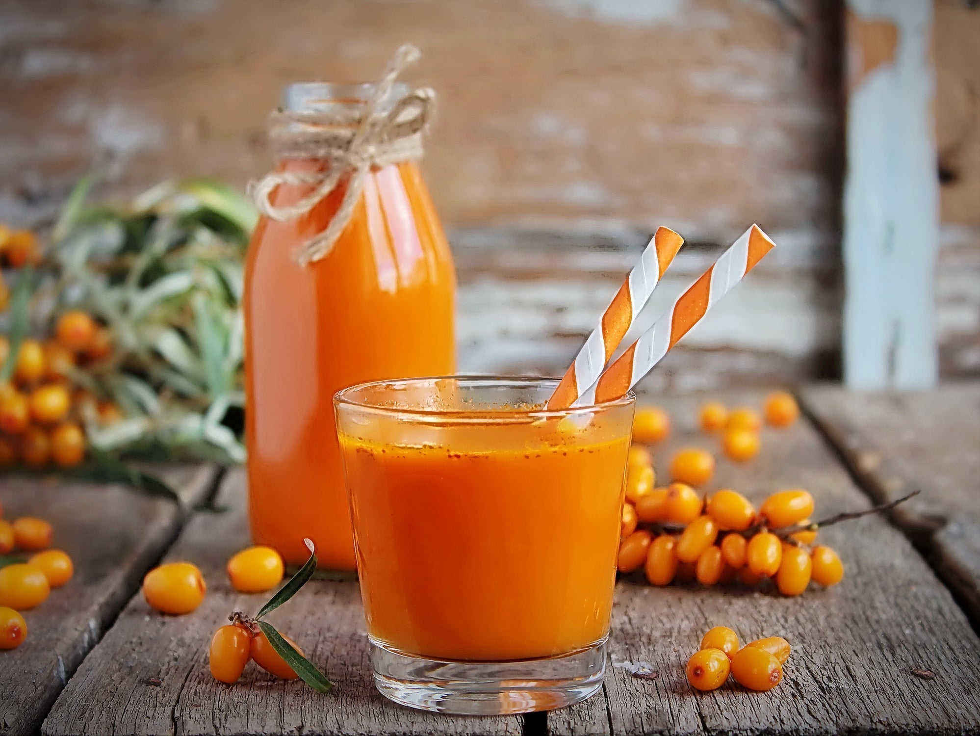 An image of a pitcher and a glass of sea buckthorn juice on a wooden table.